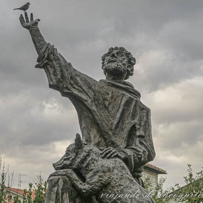 Estatua de San Francisco y el lobo en Gubbio. Un pájaro está posado en la mano del santo.