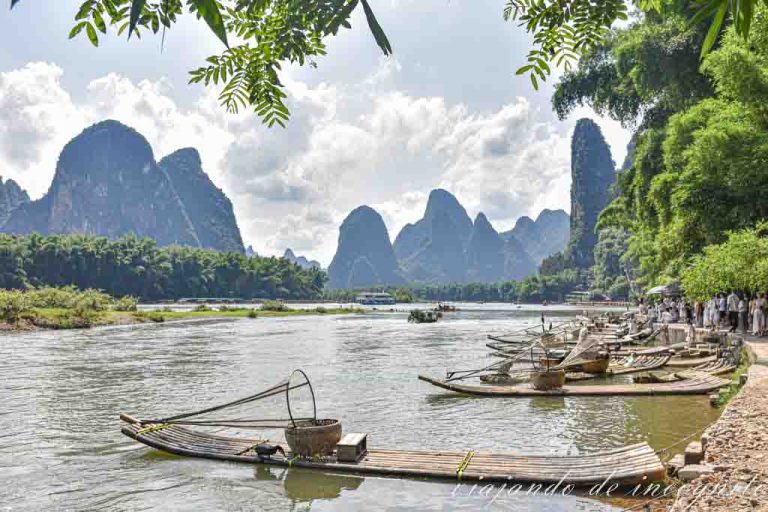 Numerosas barcas con redes y cormoranes están atracadas en Xinping con las montañas de fondo.