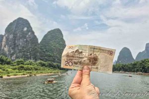 Una mano sujeta un billete de 20 yuanes frente al escenario montañoso que aparece en él.