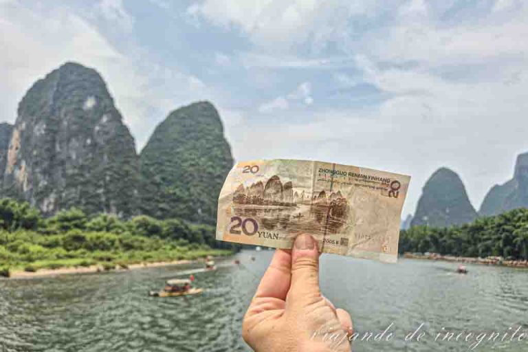 Una mano sujeta un billete de 20 yuanes frente al escenario montañoso que aparece en él.