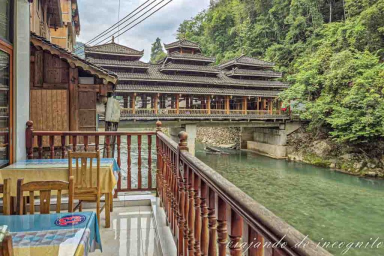 Terraza de un restaurante en Huangluo con vistas al río y a un puente de madera cubierto.