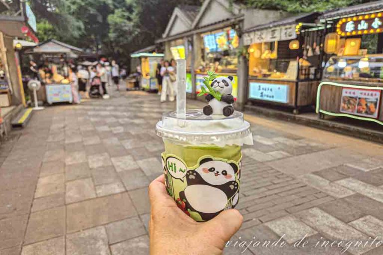 Una mano sujeta un vaso de zumo decorado con pandas. De fondo se ven los puestos de artesanía del People´s park.