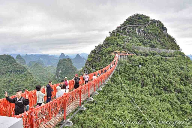 Muchas personas cruzan el puente cubierto de lazos rojos del Ruyi peak.