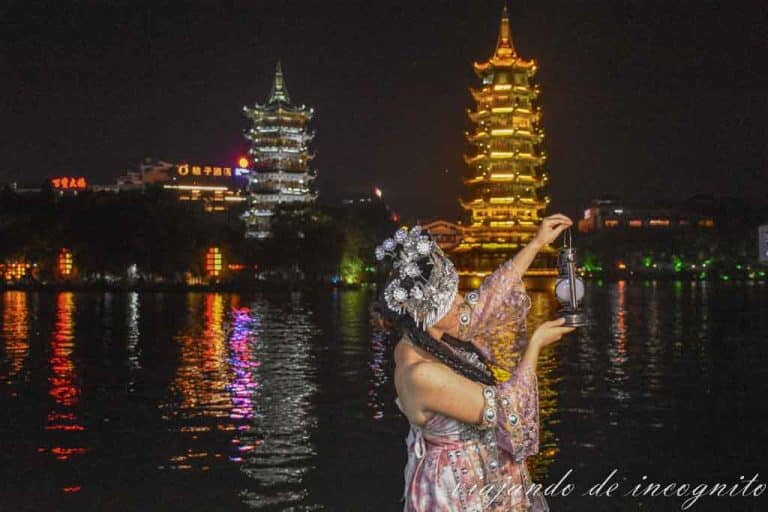 Una mujer posa con un farol vestida con un vestido tradicional frente a las pagodas del sol y la luna.