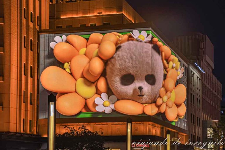 Pantalla en Wángfujing donde se ve la cabeza de un panda rodeado de flores naranjas.