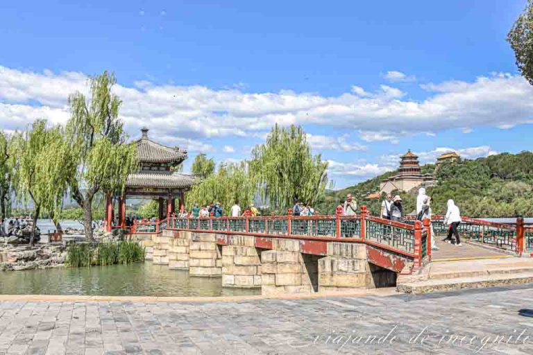 Un puente rojo cruza el lago Kunming hacia una pequeña isleta. Varias personas lo están cruzando.