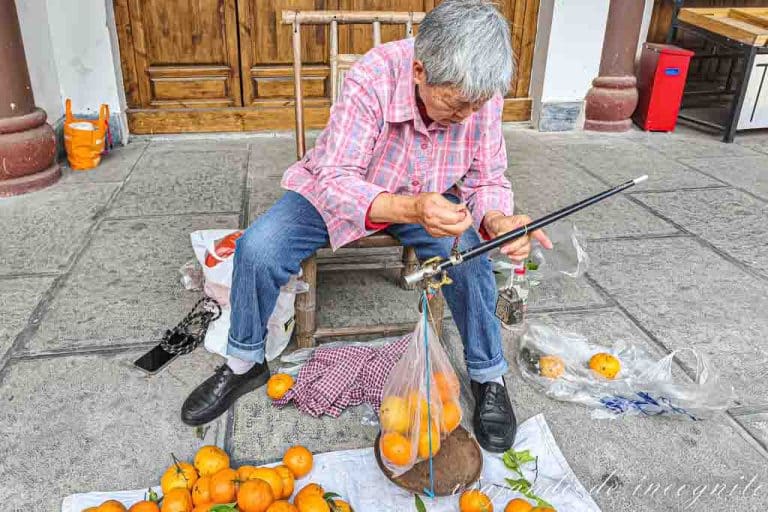 Mujer vende mandarinas en la calle y las pesa con una balanza antigua.
