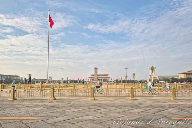 Tres ciclistas atraviesan la plaza Tiananmen frente a la bandera Nacional.