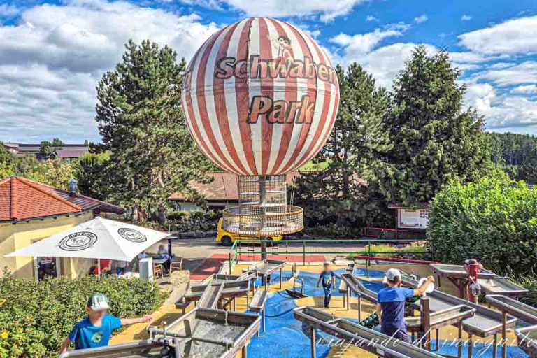 Zona de columpios de agua y al fondo un globo aerostático a rayas blancas y rojas donde está escrito Schwaben Park.