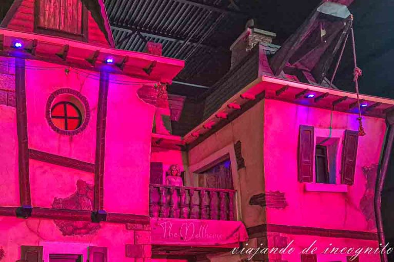 Una muñeca mira por el balcón de Villa Fiasko. Todo está iluminado con una luz rosa.
